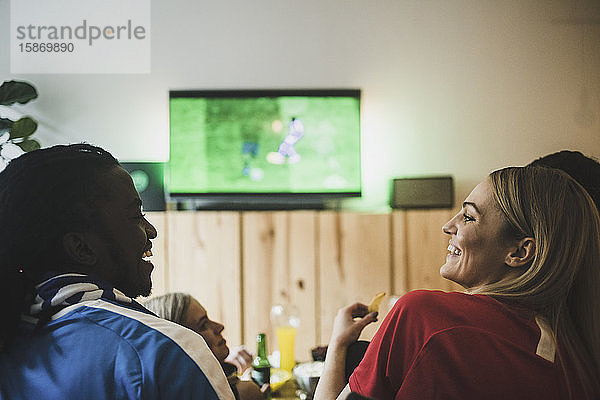 Lächelnde Männer und Frauen schauen Fußball  während sie mit Freunden zu Hause sitzen