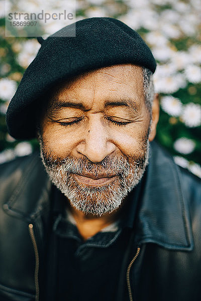 Älterer Mann mit geschlossenen Augen gegen Blumen
