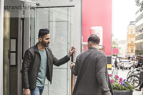 Junger Geschäftsmann verlässt das Gebäude mit einem Mitarbeiter am Eingang in der Stadt