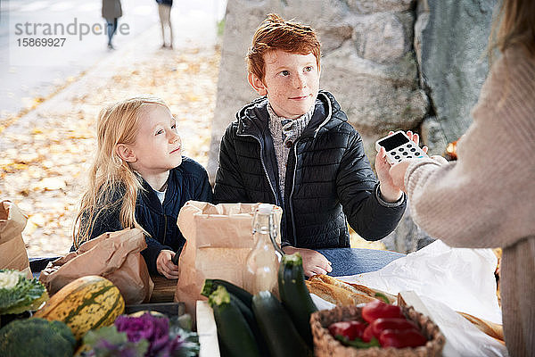 Männliche und weibliche Geschwister mit Kreditkartenleser am Marktstand