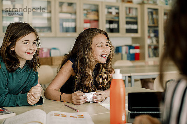 Lächelnde Studentin mit Papier  die von einem Freund im Klassenzimmer sitzt