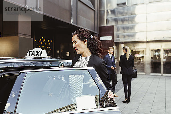 Unternehmerin steigt in Taxi ein  während ihre Mitarbeiter im Hintergrund stehen