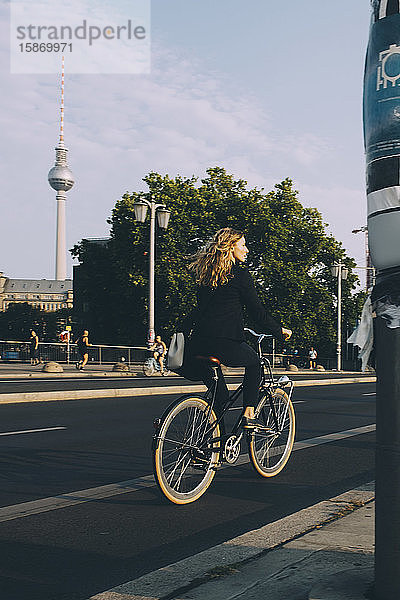 Weibliche Führungskraft in voller Länge mit dem Fahrrad auf der Straße in der Stadt gegen den Himmel
