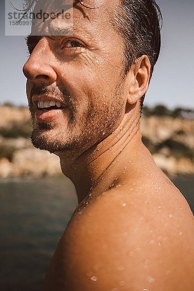 Seitenansicht eines Mannes ohne Hemd  der weg schaut  während er an einem sonnigen Tag Urlaub am Strand macht