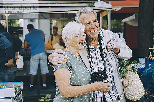Lächelndes älteres Ehepaar mit Arm um den Arm auf dem Markt in der Stadt stehend