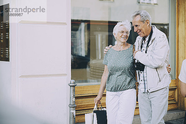 Lächelndes älteres Ehepaar mit umarmtem Arm auf dem Bürgersteig in der Stadt