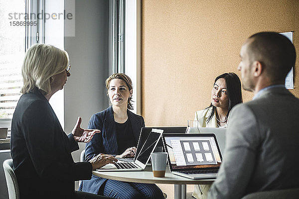 Leitende Geschäftsfrau bespricht Strategien mit Kollegen  während sie im Sitzungssaal sitzt