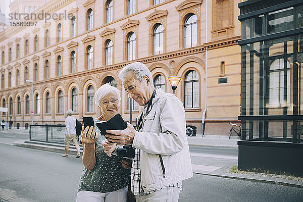 Lächelnder älterer Tourist und Touristin mit Smartphone bei Stadterkundung