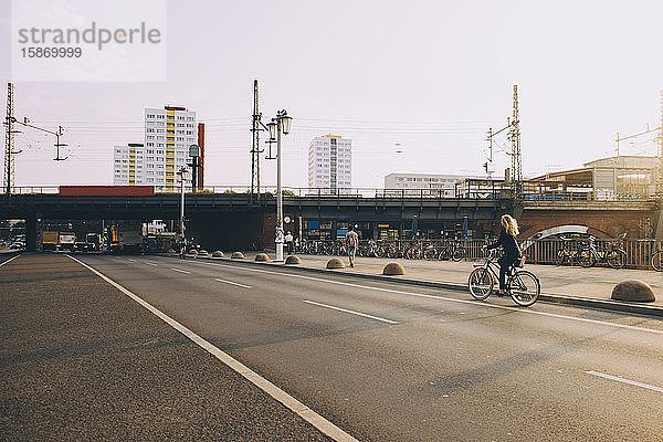 Seltener Anblick einer Geschäftsfrau  die auf der Straße in der Stadt mit dem Fahrrad gegen den Himmel fährt