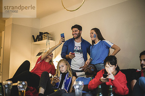 Männer und Frauen nutzen Smartphones  während sie sich zu Hause ein Fußballspiel ansehen