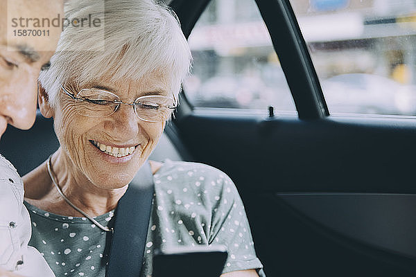 Lächelnde ältere Frau zeigt einem Mann ihr Handy  während sie im Auto sitzt