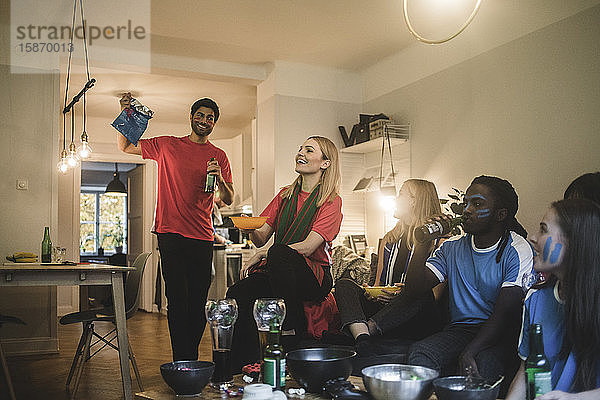 Lächelnde männliche und weibliche Freunde sehen sich im Wohnzimmer ein Fußballspiel an