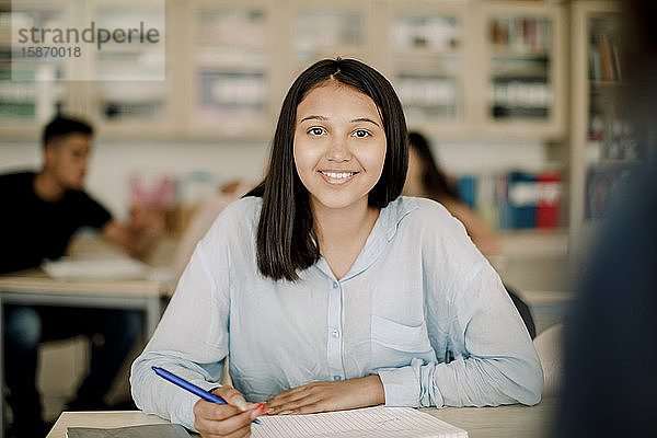 Porträt einer lächelnden Teenagerin beim Lernen am Tisch im Klassenzimmer