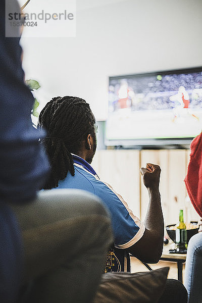 Rückansicht eines Mannes  der sich zu Hause mit einem Freund ein Fußballspiel ansieht