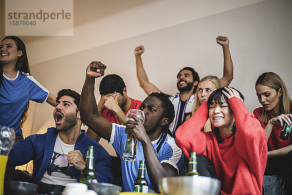 Multiethnische Freunde sehen sich ein Fußballspiel an  während sie zu Hause an der Wand sitzen