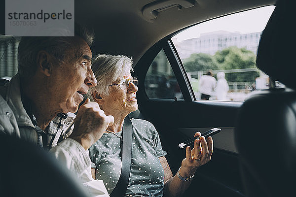 Ältere Frau hält Handy in der Hand  während sie mit Mann im Auto sitzt