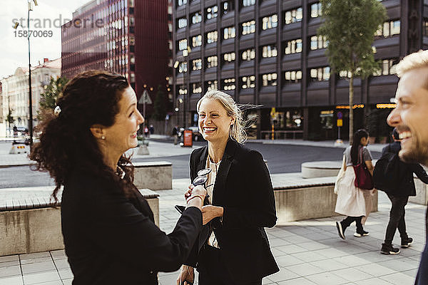 Unternehmerin lächelt mit ihren Mitarbeitern  während sie im Freien steht