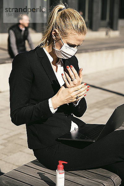 Geschäftsfrau  die mit Laptop-Waring-Gesichtsmaske und Handdesinfektionsmittel arbeitet