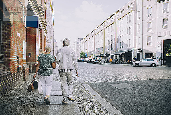 Rückansicht eines älteren Ehepaars  das im Urlaub in der Stadt auf dem Bürgersteig geht