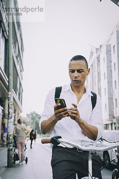 Geschäftsmann benutzt Mobiltelefon beim Fahrradfahren auf dem Bürgersteig in der Stadt
