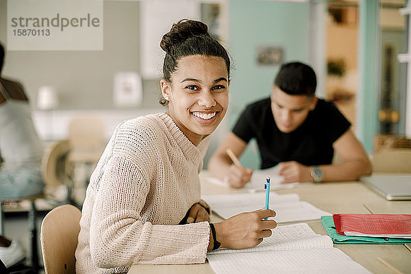 Porträt eines lächelnden Teenagers  der im Klassenzimmer sitzt und lernt