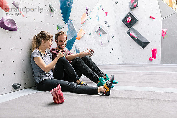 Frau zeigt lächelndem männlichen Freund Mobiltelefon  während sie im Fitnessstudio sitzt