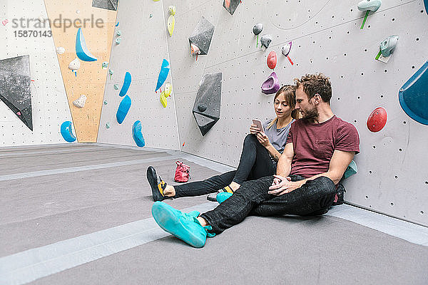 Frau zeigt einem Freund ein Smartphone  während sie im Fitnessstudio sitzt