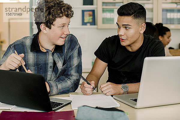 Männliche Studenten sprechen  während sie im Klassenzimmer am Tisch sitzen