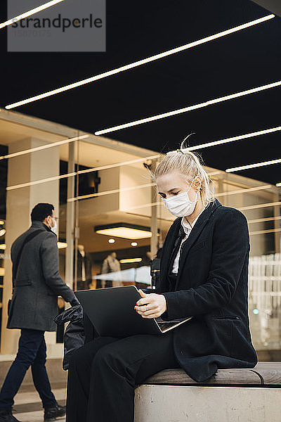 Geschäftsfrau mit Gesichtsmaske sitzt mit Laptop im Freien