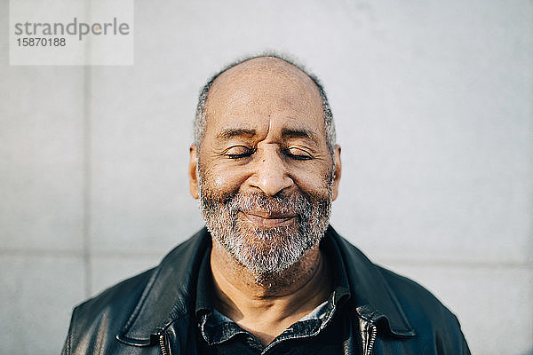 Lächelnder älterer Mann mit geschlossenen Augen an der Wand