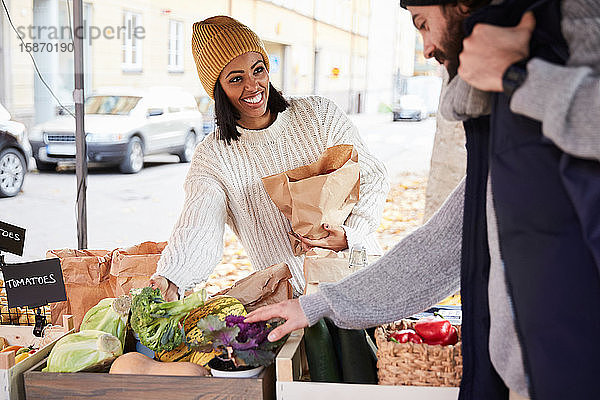 Lächelnde Frau kauft frisches Gemüse von männlichem Marktverkäufer am Obststand