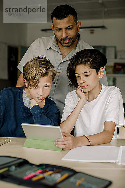 Männlicher Tutor mit Studenten  die ein digitales Tablet benutzen  während sie im Klassenzimmer sitzen