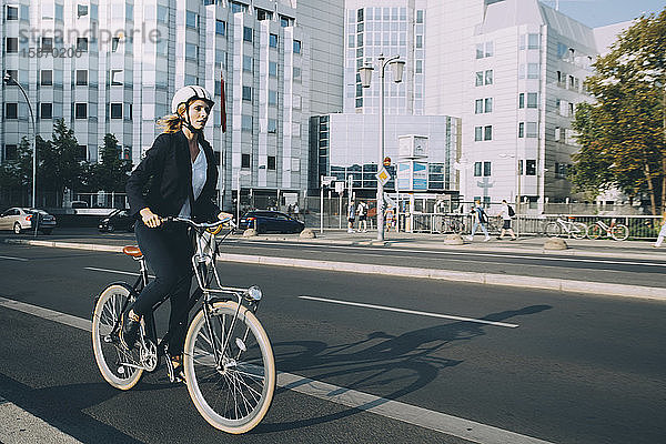 Junge Frau in voller Länge mit Helm beim Fahrradfahren auf der Straße in der Stadt
