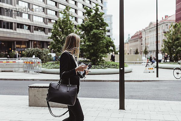 Seitenansicht einer Unternehmerin mit einem Smartphone auf dem Bürgersteig