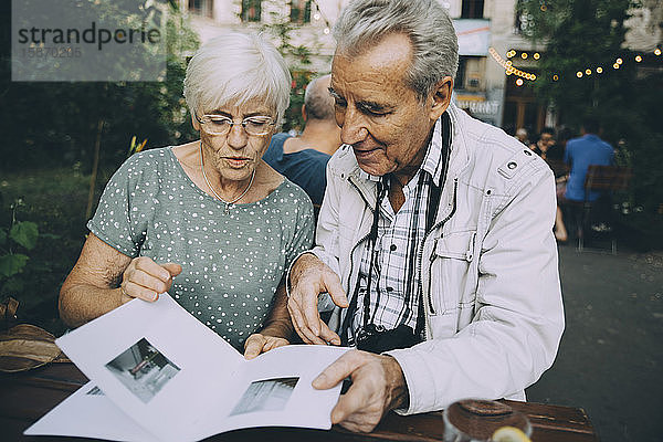 Älterer Mann und ältere Touristin schauen sich Bilder in einem Buch an  während sie im Restaurant sitzen