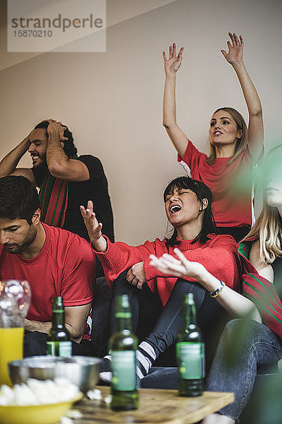 Traurige männliche und weibliche Fans sehen Fußballspiele  während sie zu Hause auf dem Sofa sitzen