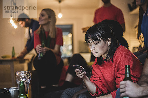 Junge Frau benutzt Mobiltelefon  während sie mit Freunden zu Hause sitzt