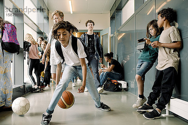 Männlicher Schüler  der in der Mittagspause auf dem Schulkorridor mit einem Sportball spielt