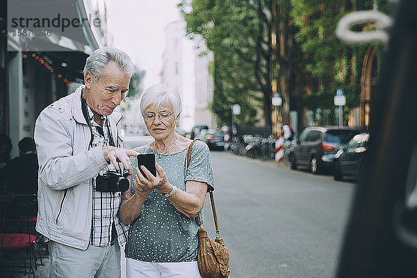 Ältere Männer und Frauen benutzen ein Smartphone  während sie in der Stadt auf dem Bürgersteig stehen