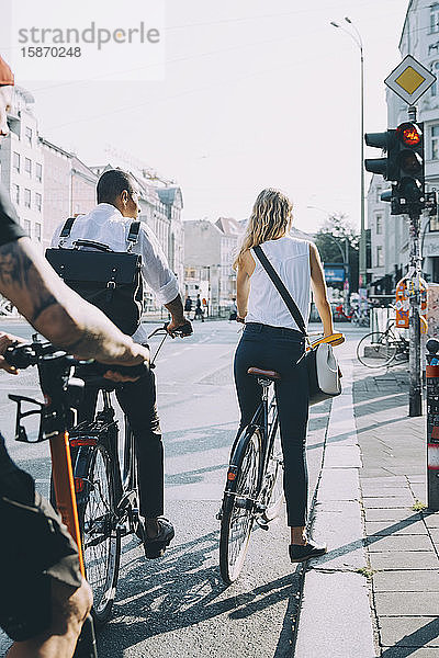 Rückansicht von Geschäftskollegen  die mit dem Fahrrad an einem Signal in der Stadt stehen