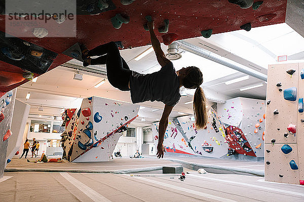 Frau übt Wandklettern in Turnhalle