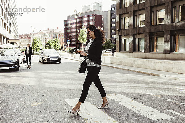 Geschäftsfrau schaut beim Überqueren der Straße auf ein Smartphone