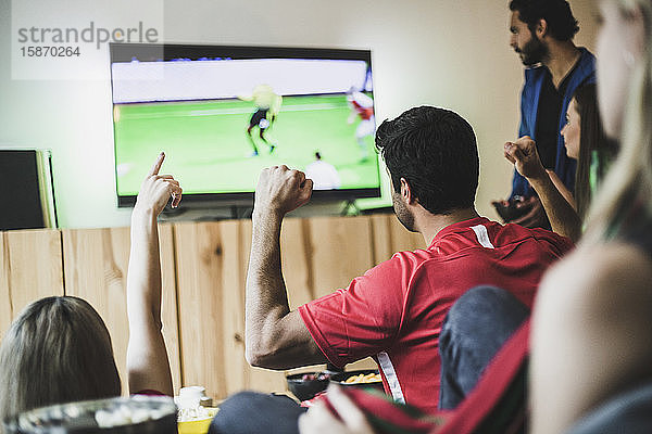Freunde und Freundinnen sehen sich zu Hause ein Fußballspiel im Fernsehen an