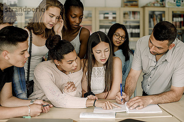 Professor unterrichtet männliche und weibliche Studenten  während er sich im Klassenzimmer über den Tisch lehnt