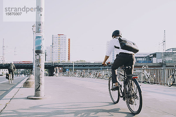 Rückansicht eines Geschäftsmannes auf dem Fahrrad auf dem Bürgersteig vor klarem Himmel in der Stadt