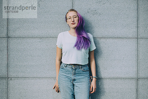 Porträt eines an der Wand stehenden Teenagers mit lila Haaren