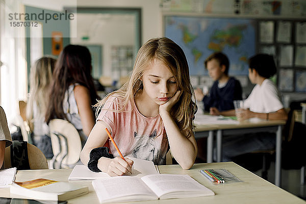 Studentin mit Hand am Kinn lernt aus einem Buch  während sie im Klassenzimmer sitzt