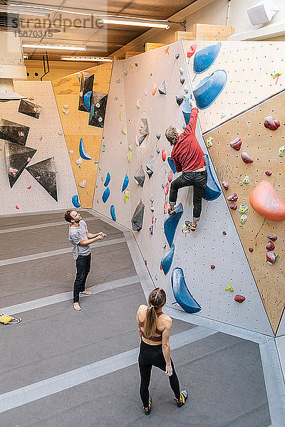 Hochwinkelansicht männlicher und weiblicher Studenten  die auf die Kletterwand eines reifen Trainers in einer Turnhalle blicken