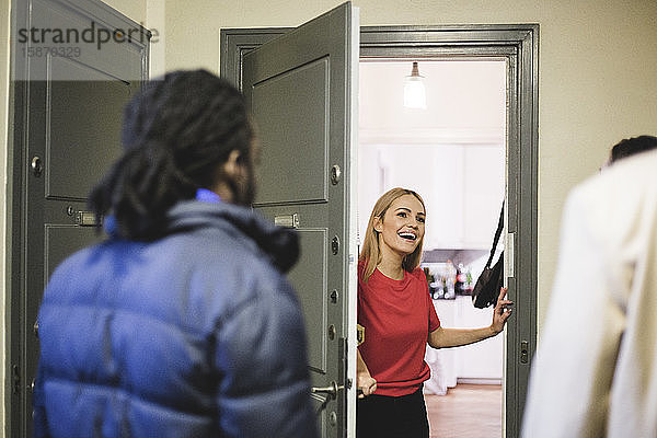 Fröhliche Frau begrüßt Freunde  während sie an der Tür steht