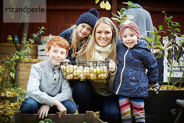Porträt einer lächelnden Mutter mit kauerndem Kartoffelkorb von Kindern im Hof